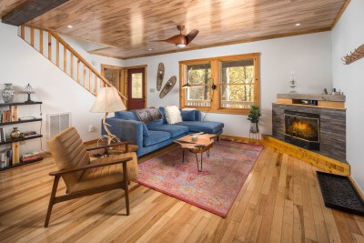 Charming, wood-accented living room centered on a stone fireplace, with pine ceilings, exposed beams overhead, and warm wood finishes throughout — a relaxed, welcoming space to unwind after a day spent exploring the mountains.