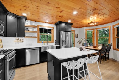 A renovated kitchen with black cabinetry, new stainless appliances, and an island that seats the whole group. The dining table is just past the arch.