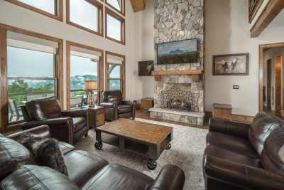 Two stories of windows pull the mountains straight into the great room, where a stone fireplace and deep leather seating make the whole group want to stay put.