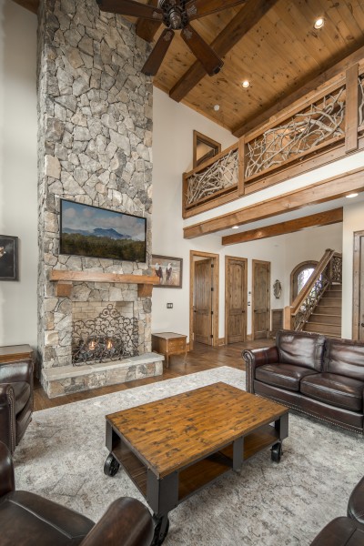 The stone chimney climbs a full two stories to the vaulted pine ceiling, with the branch-railing loft looking down over the room.