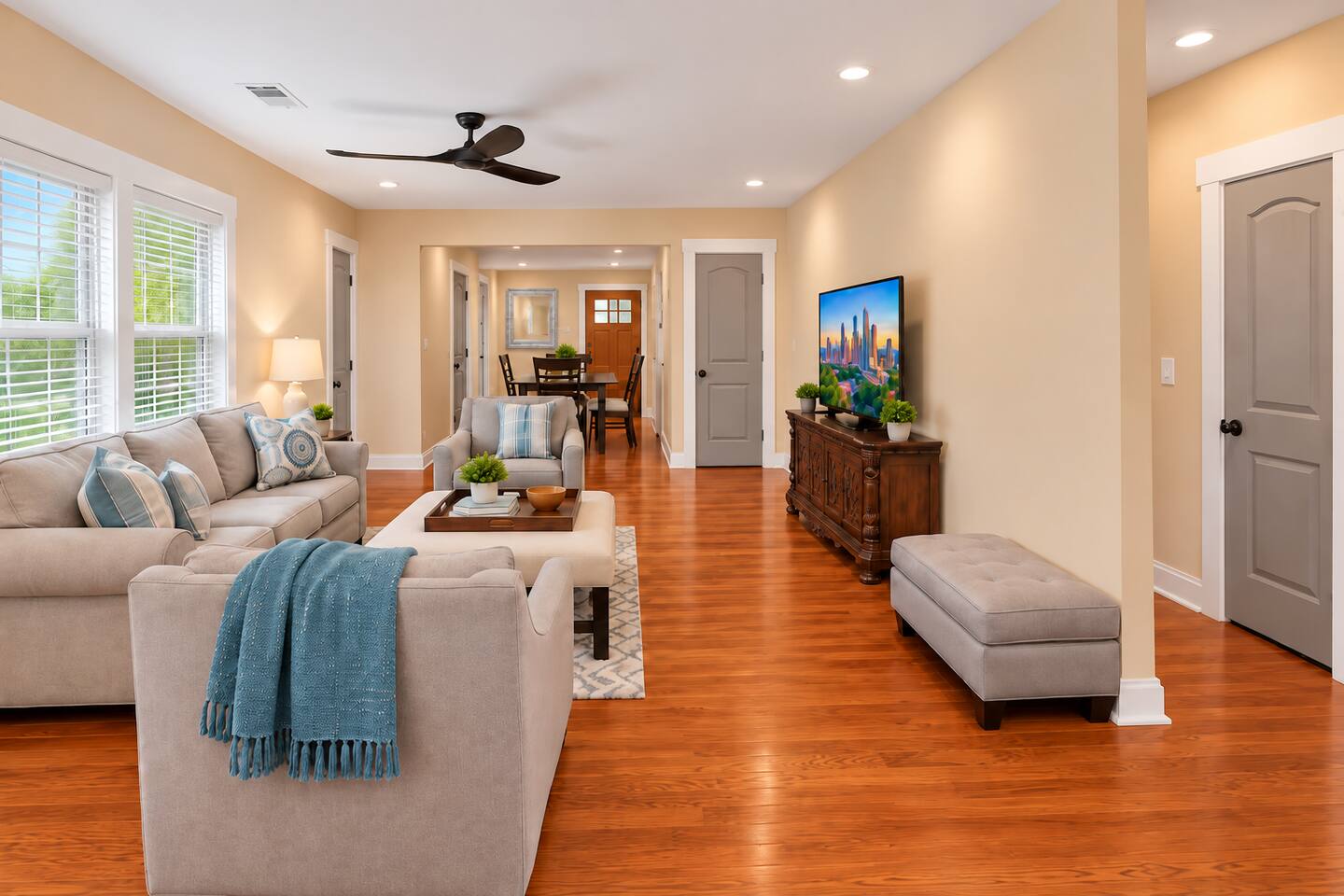 Sunlit living room featuring cushy sofas, hardwood flooring, and seamless flow into the dining area.