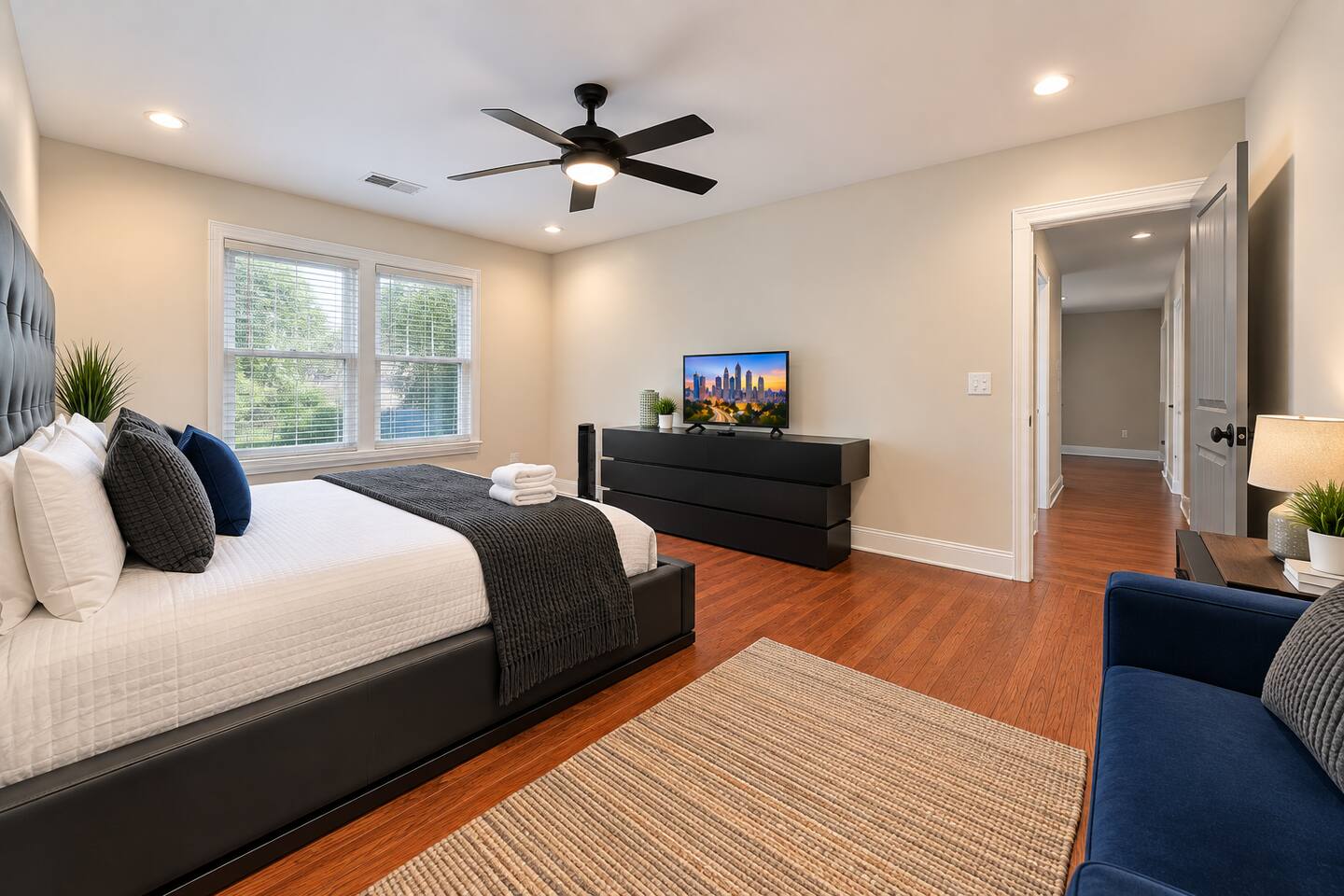 Bright and stylish bedroom with a king bed, warm hardwood flooring, ceiling fan, and plush accents.