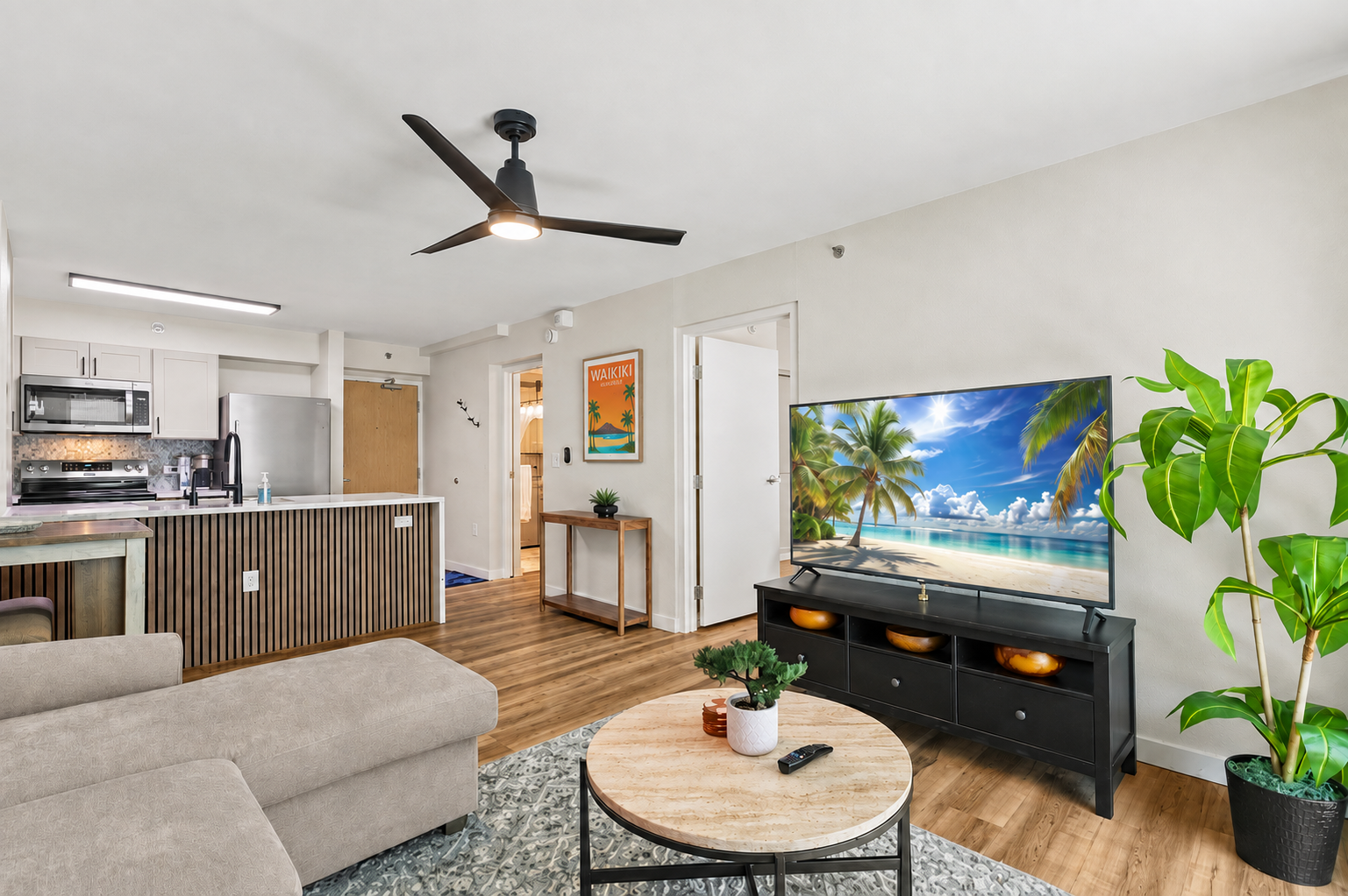 Bright open living space with modern kitchen, big TV, and tropical touches