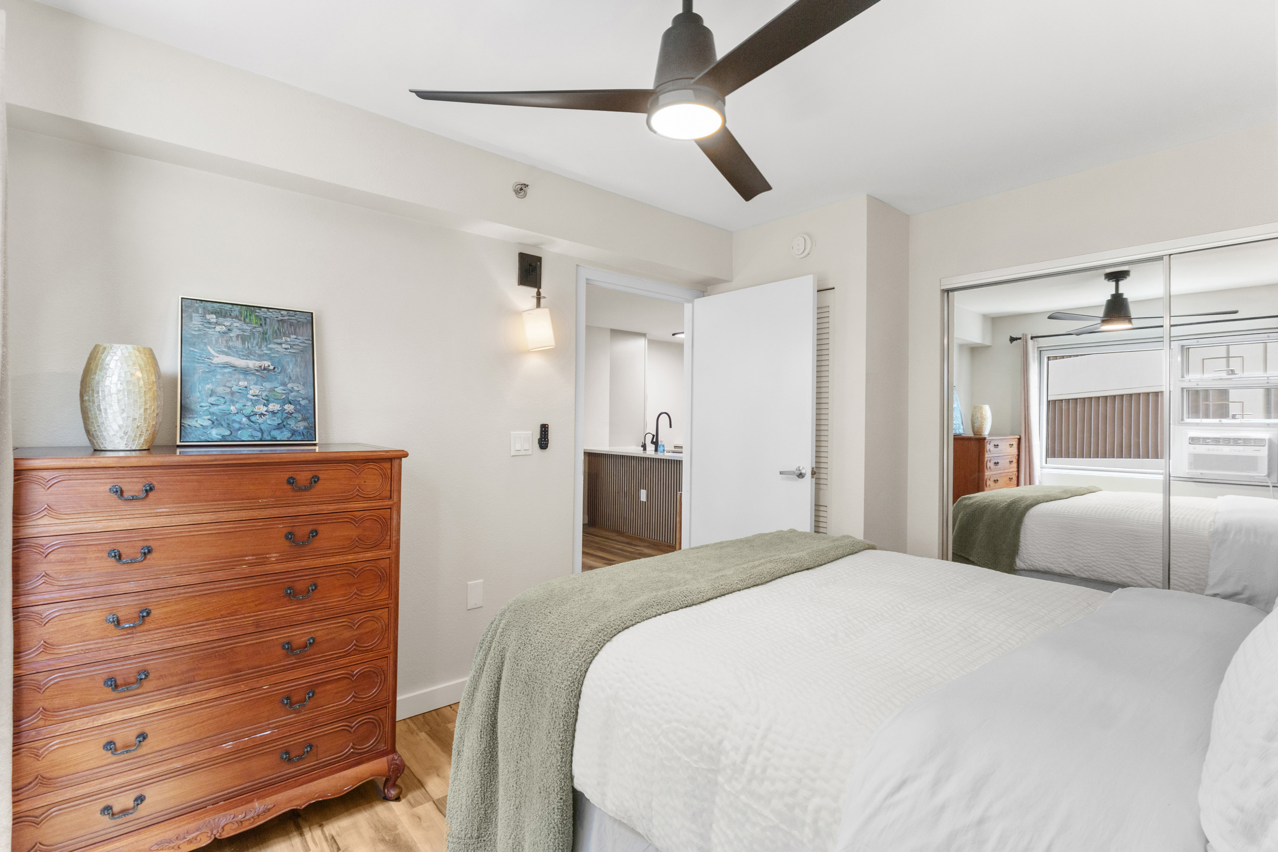 Bright, cozy bedroom with mirrored closet, ceiling fan, and warm wood accents