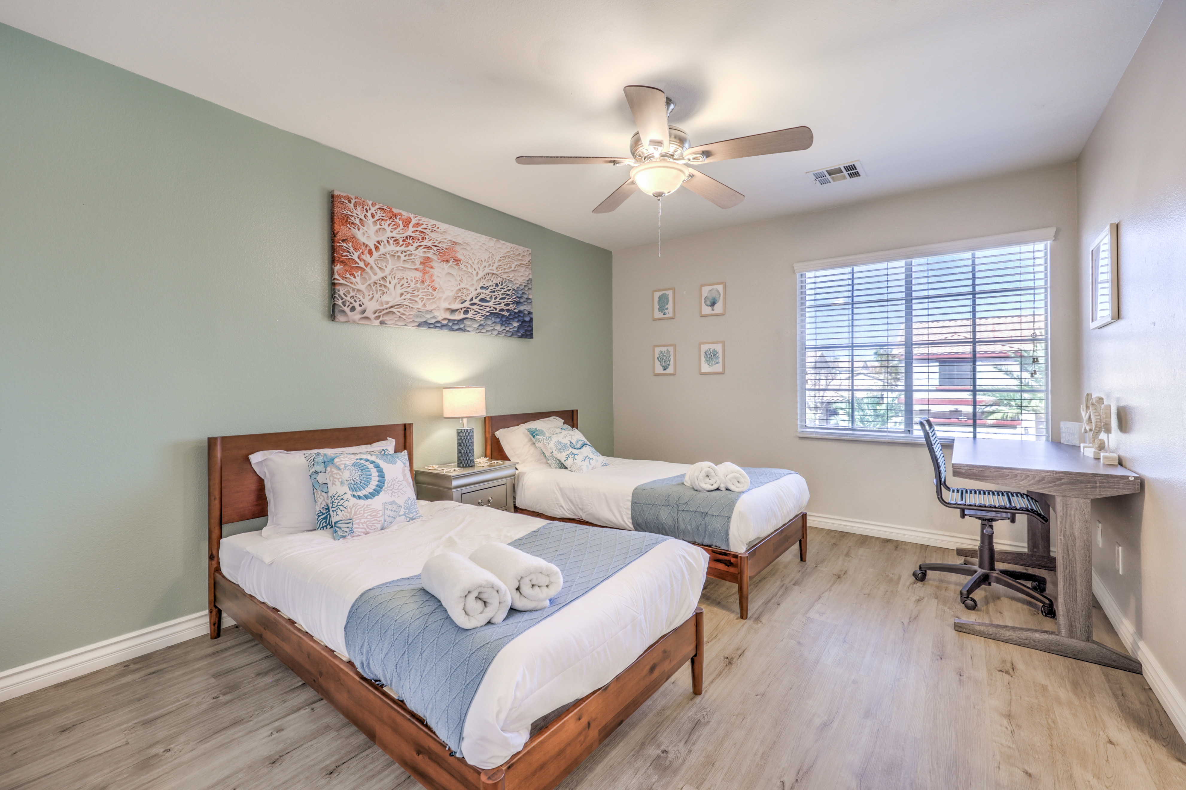 Bright twin bedroom with workspace, natural light, and coastal decor