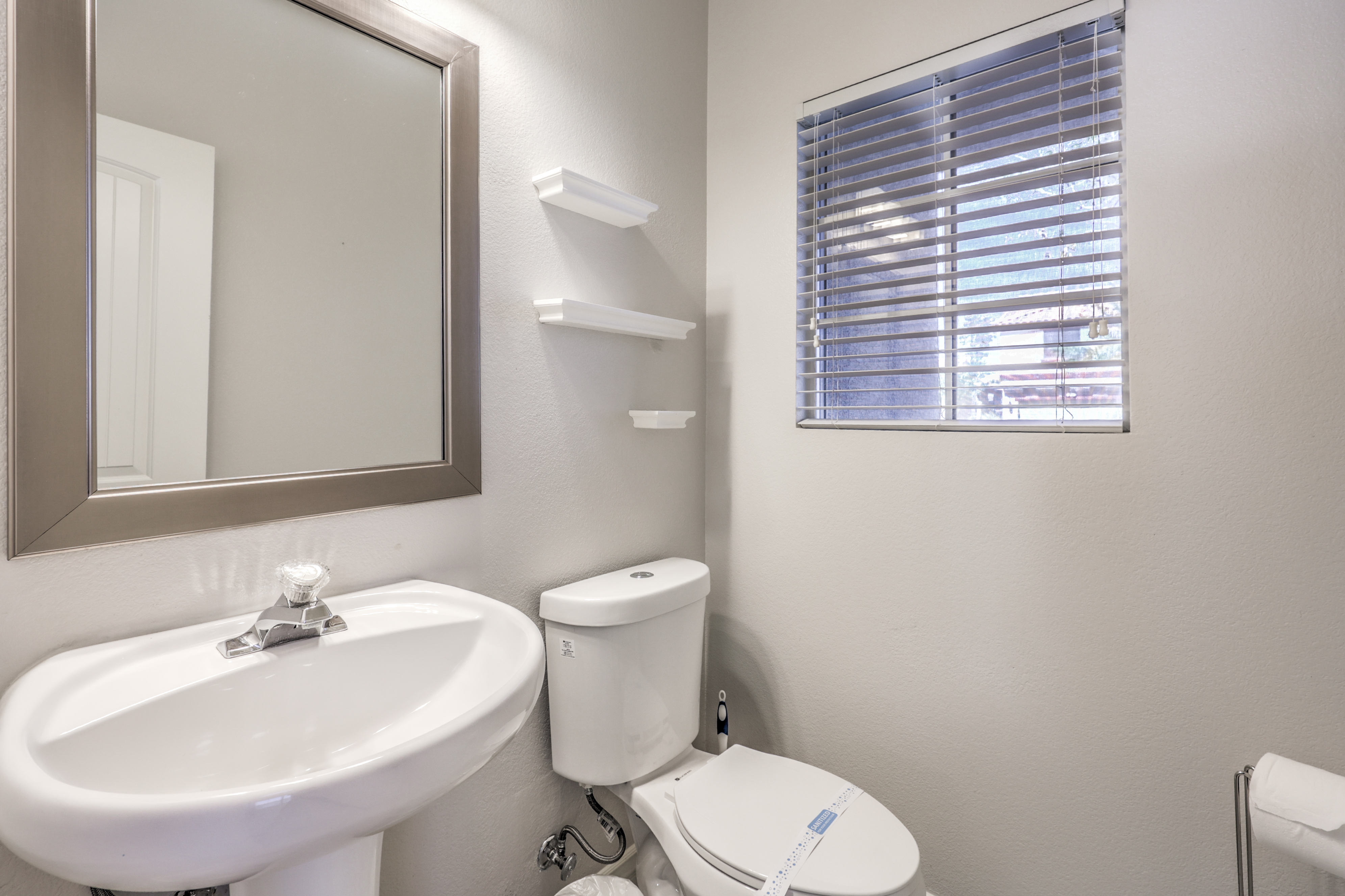 Bright bathroom with natural light, pedestal sink, and handy wall shelves