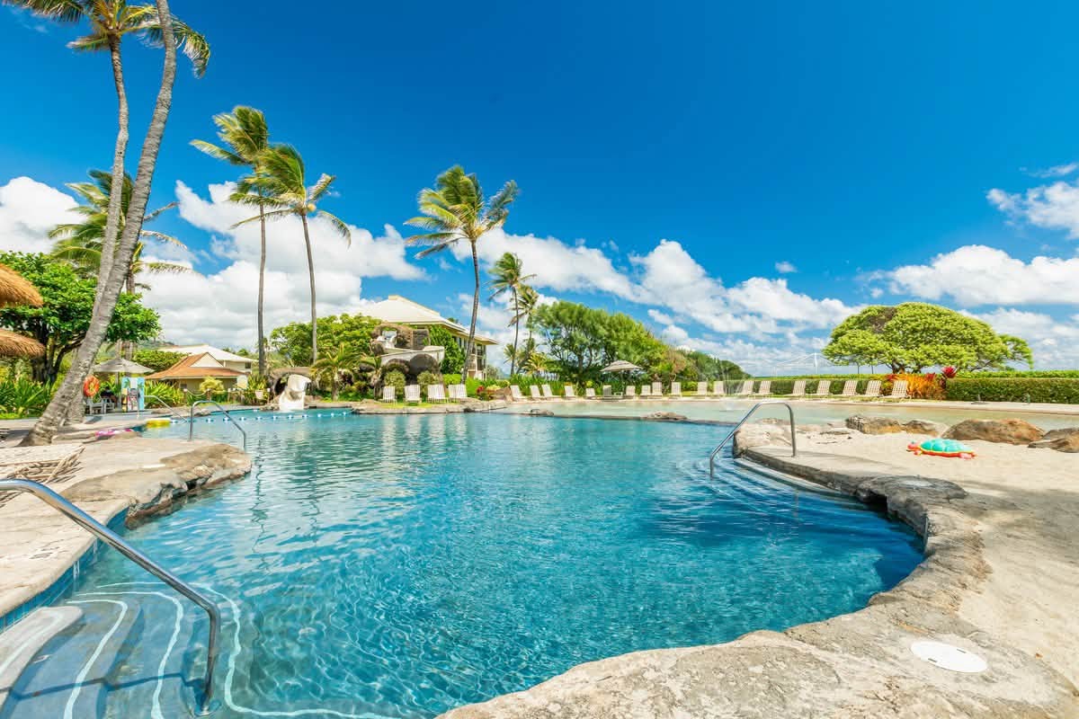 Resort-style tropical pool with palms, loungers, and sunny island vibes