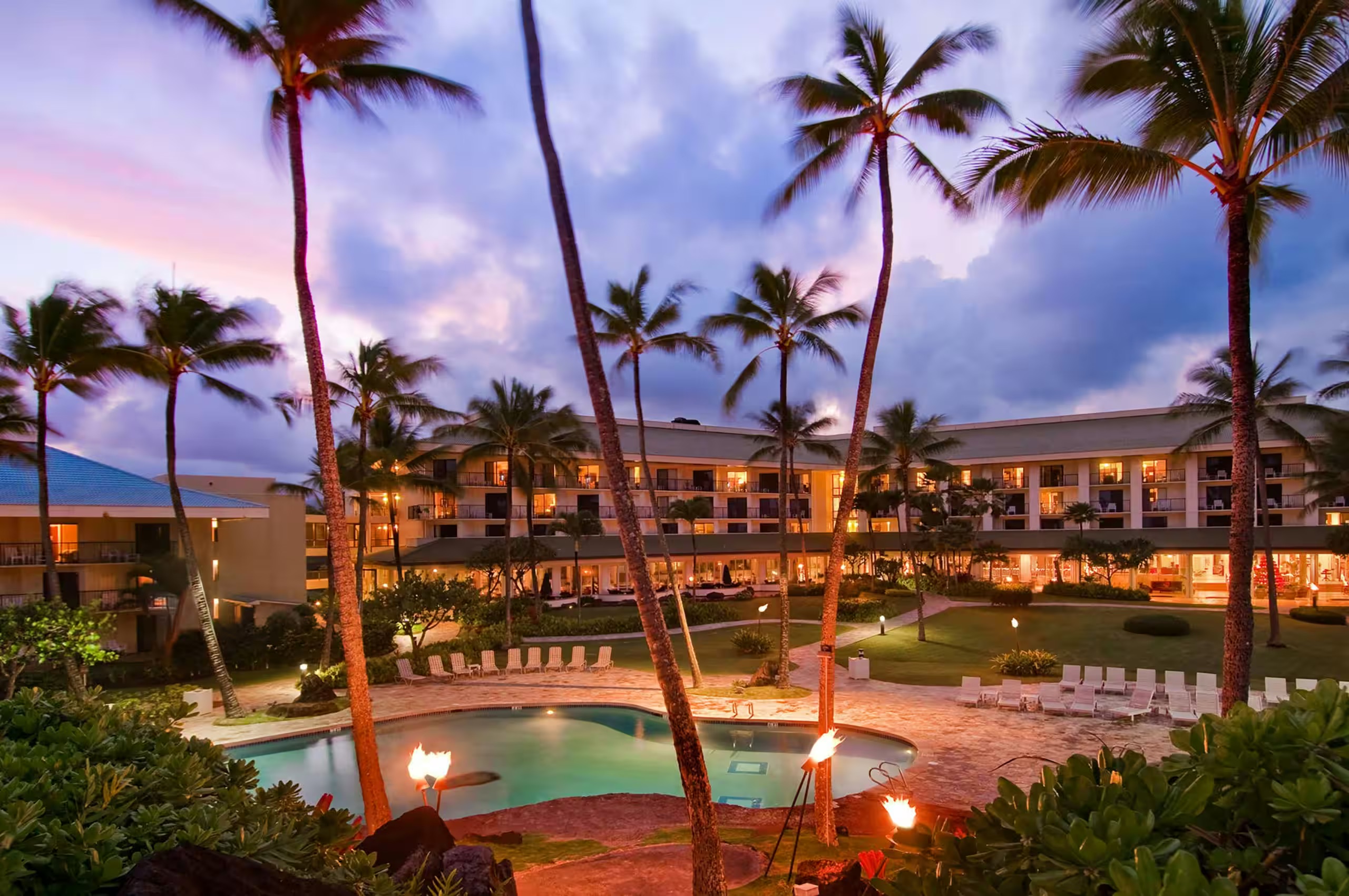 Tropical resort pool at sunset with palms, torches, and glowing courtyard