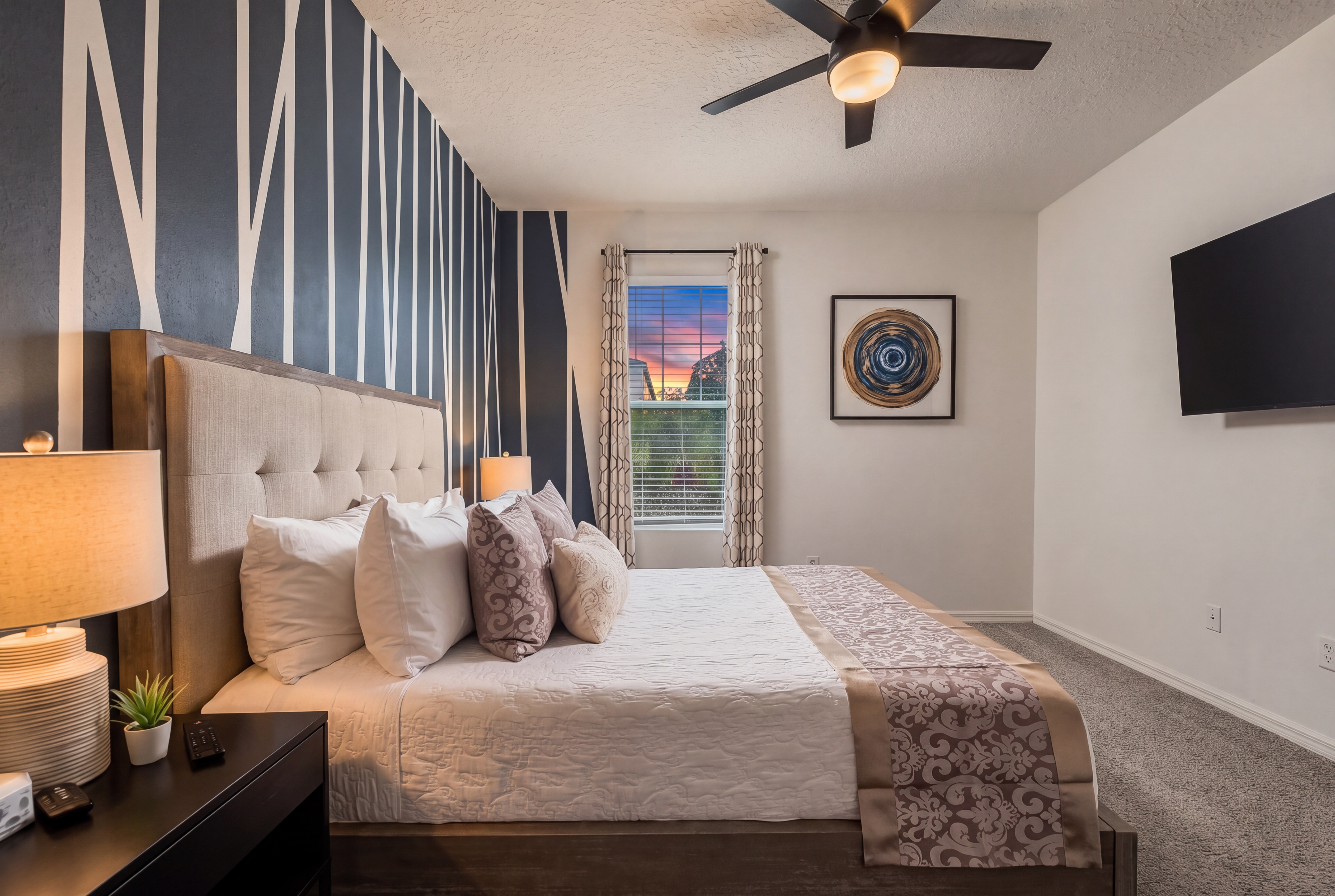 Stylish bedroom on 1st Floor with Queen size bed, with bold accent wall, TV, and sunset window view