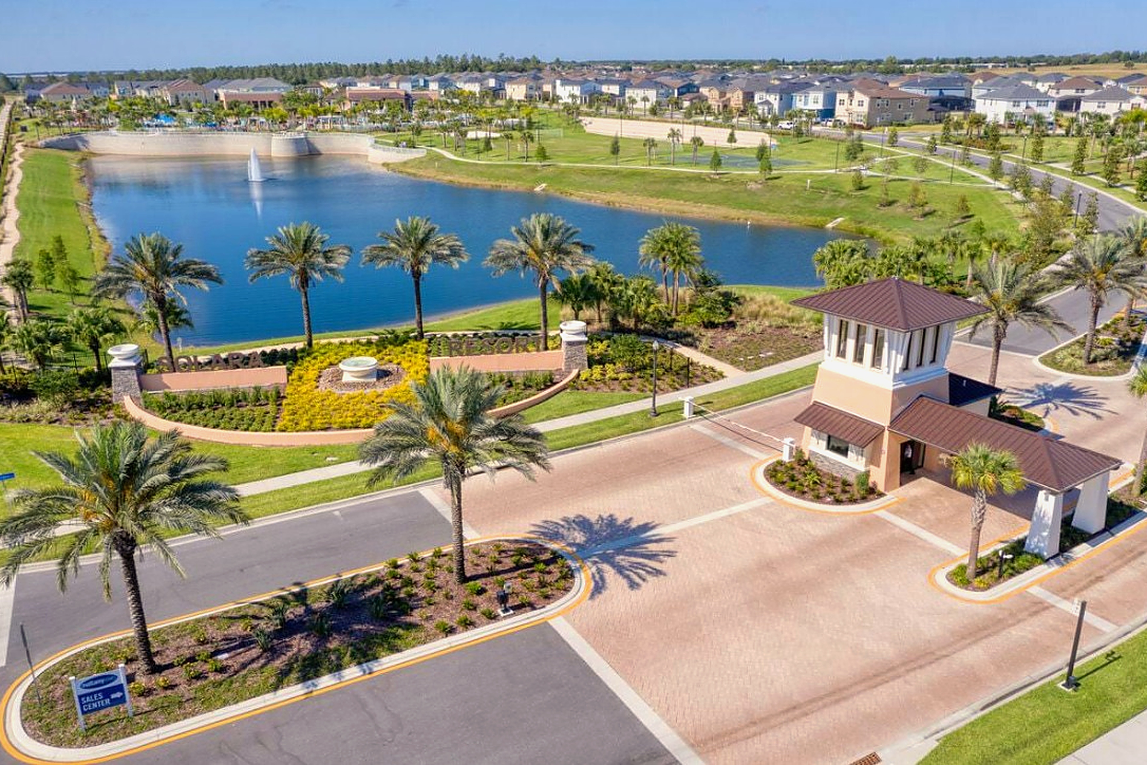 Resort-style gated entrance with lake views, palms, and manicured grounds