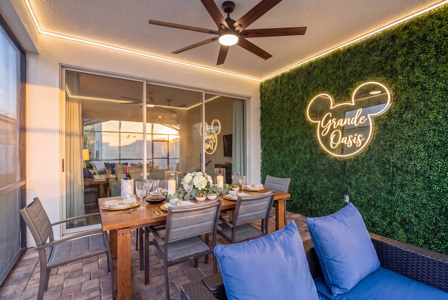 Covered lanai with outdoor dining, lounge seating, and the glowing Grande Oasis sign — built for sunset dinners.