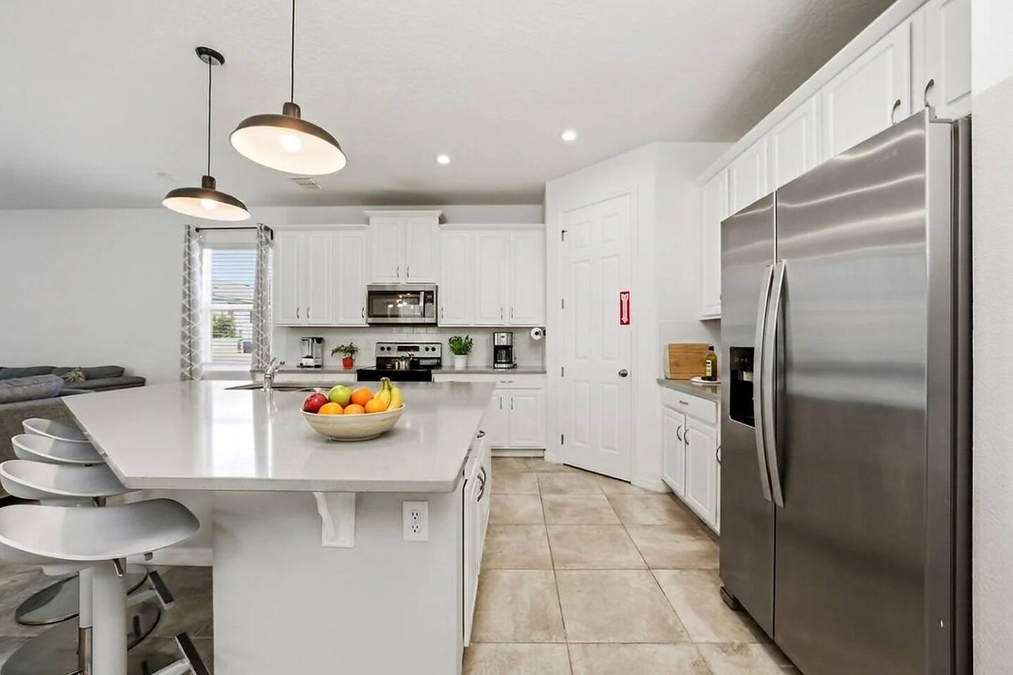 A bright, fully equipped kitchen with full-size stainless appliances, a French-door refrigerator, stone countertops, and a pantry. Island seating plus full place settings — everything you need to cook for the group.