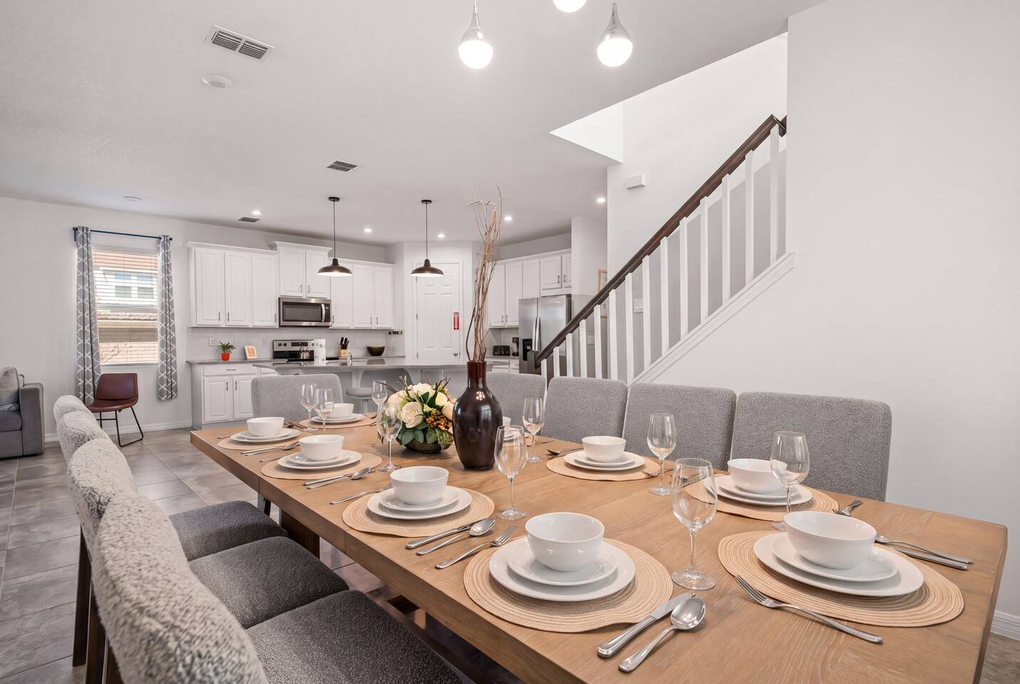 An open dining space that seats ten, flowing into the kitchen and living area so the whole group stays together — plus island counter seating. Fully stocked with plates, glasses, and silverware for a large party, ready for a big family dinner.