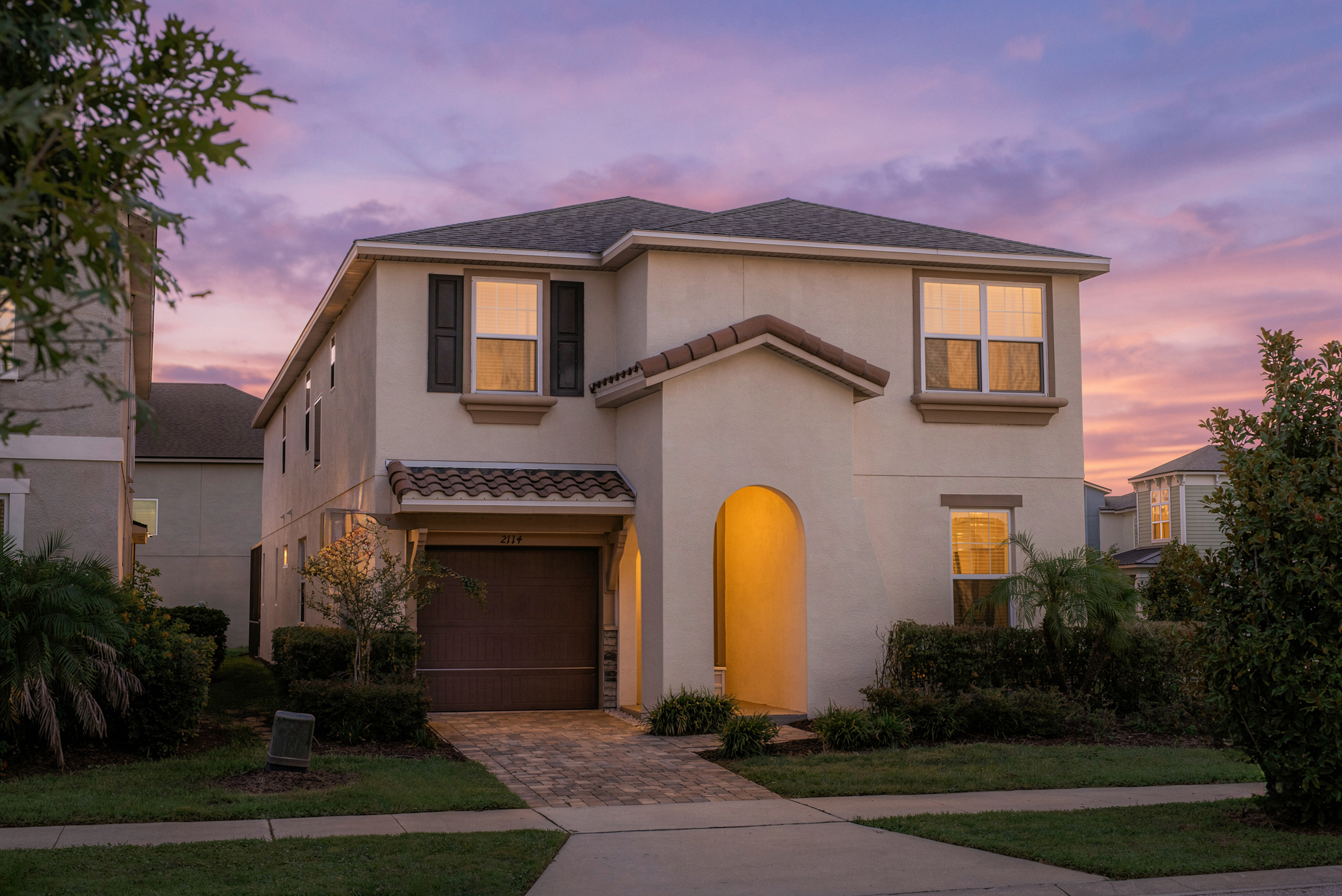 Grande Oasis at twilight — a spacious home in gated Solara Resort, just minutes from Disney.  A large two-story stucco home that sleeps up to 16, at dusk with warm interior lights glowing and a colorful sunset sky.