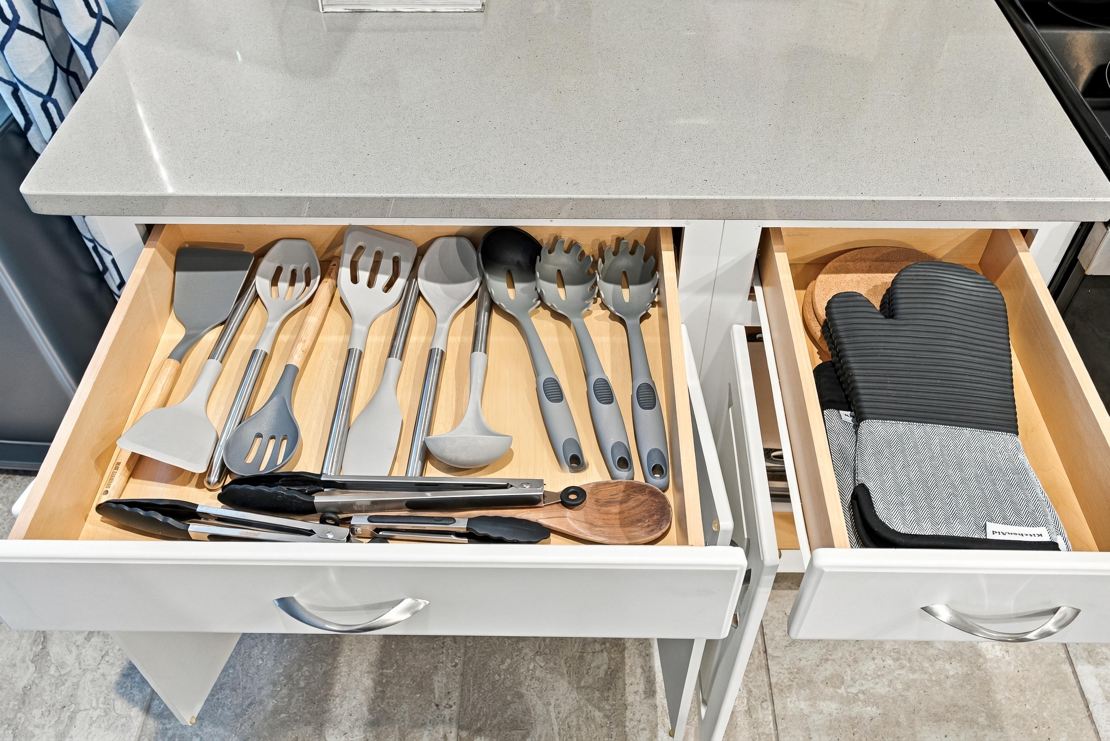 Well-stocked kitchen drawers with cooking tools and oven mitts
