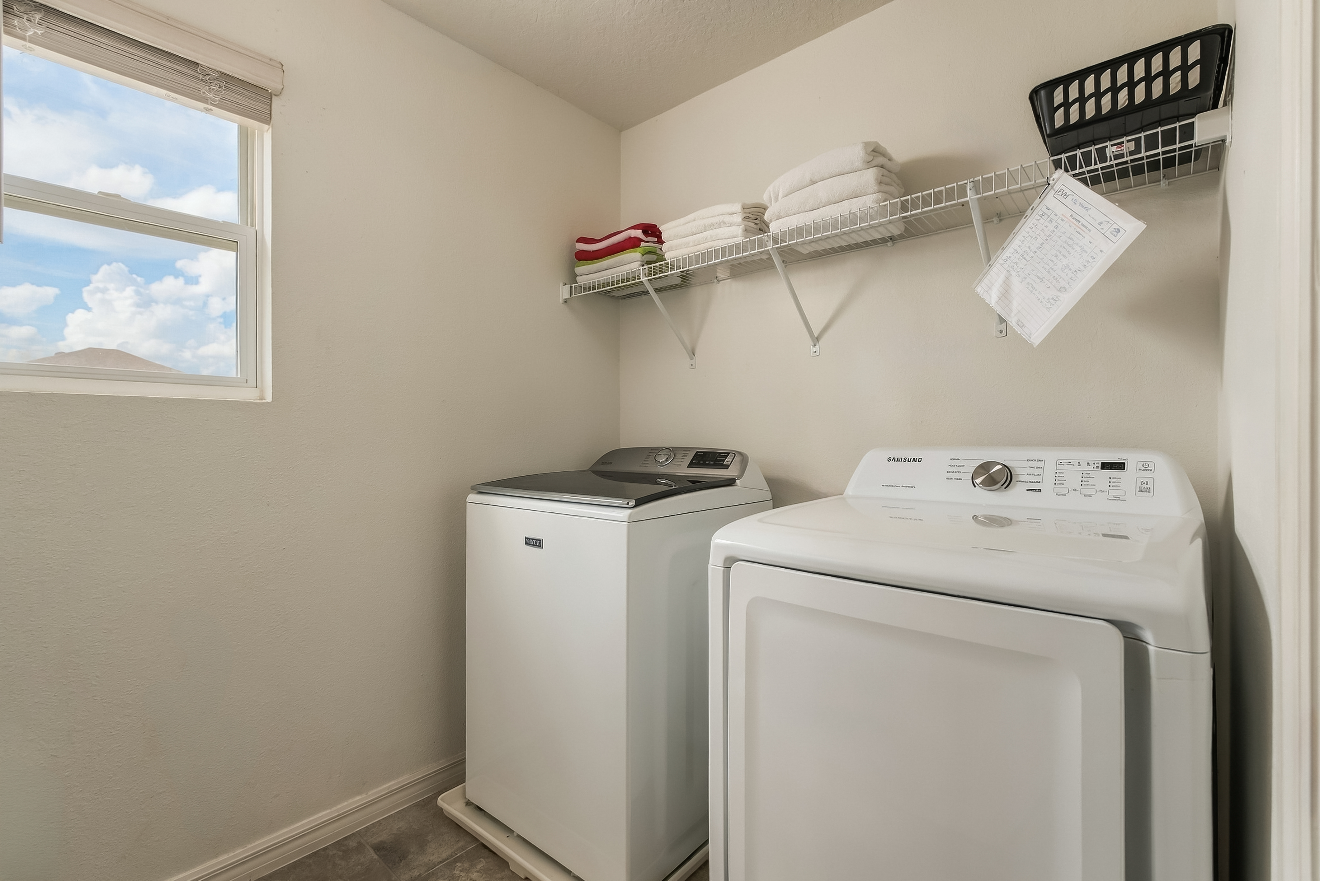 Bright laundry room with full-size washer, dryer, and handy storage shelf