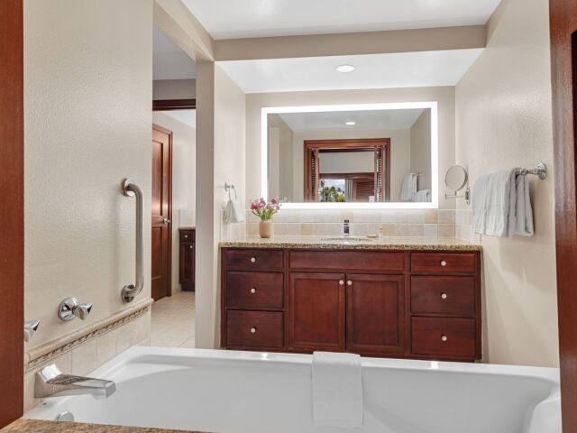 Spa-like bathroom with soaking tub, granite vanity, and glowing mirror
