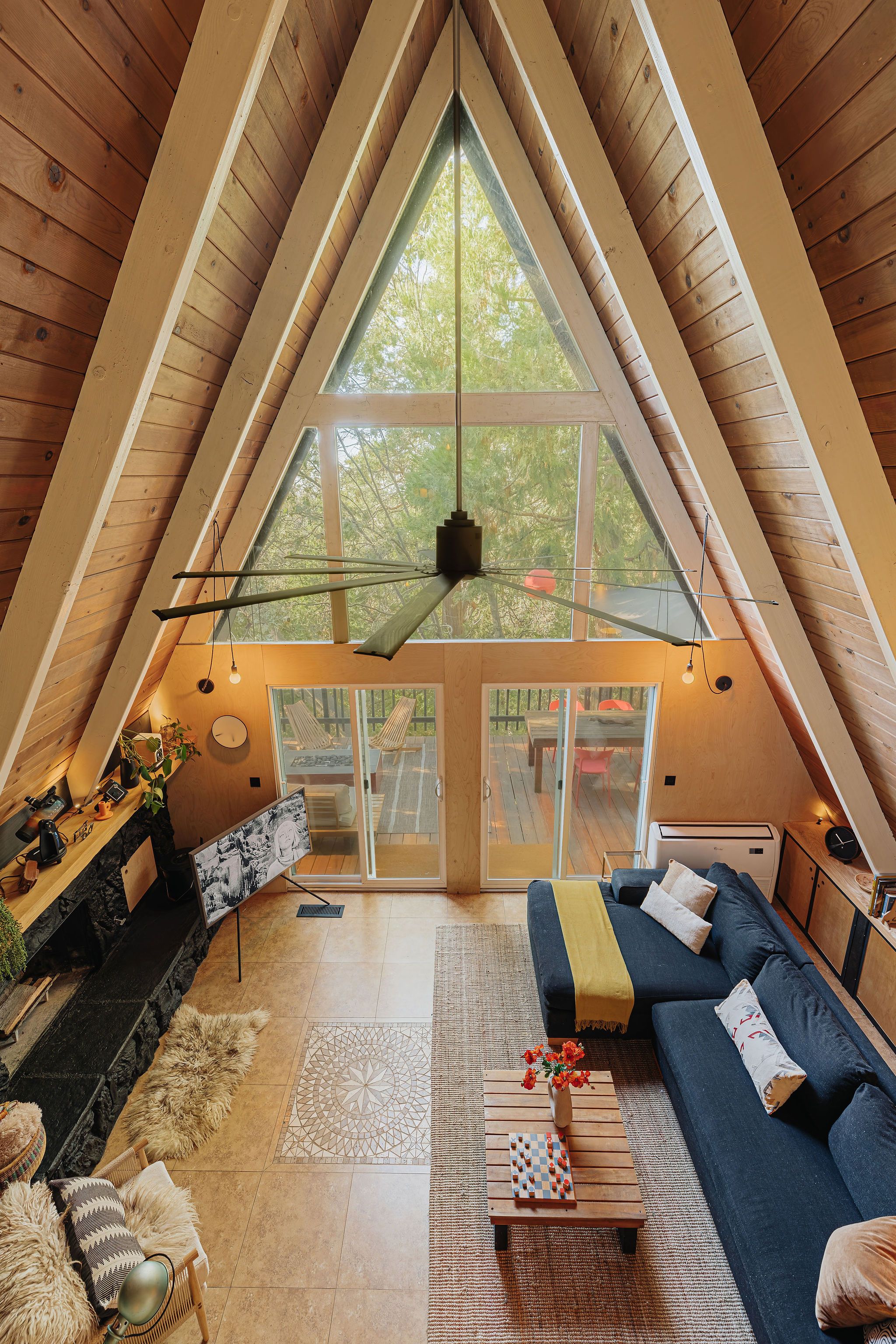 Bright A-frame lounge with soaring windows, fireplace, and tree-view deck