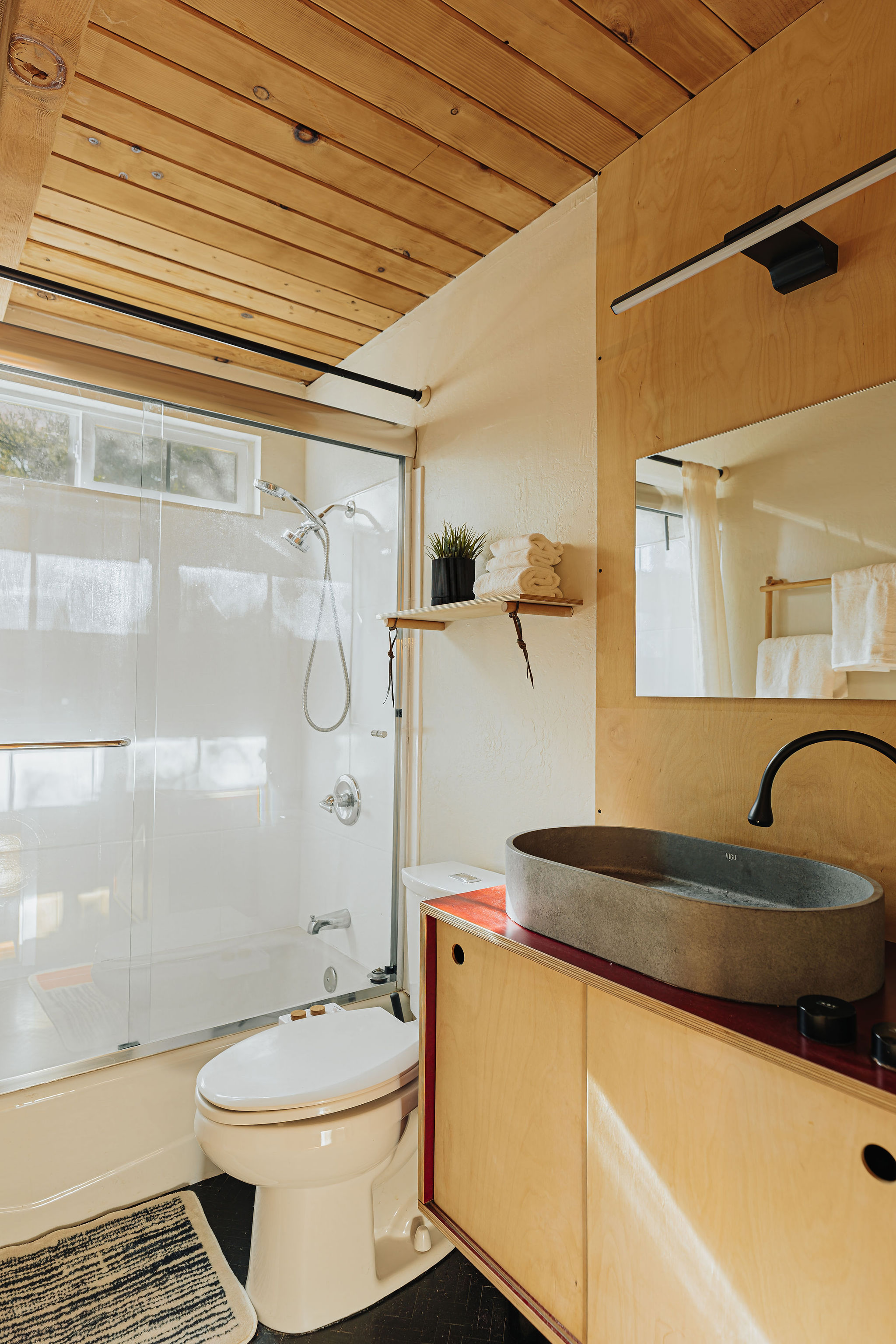 Bright modern bath with wood accents, vessel sink, and glass shower