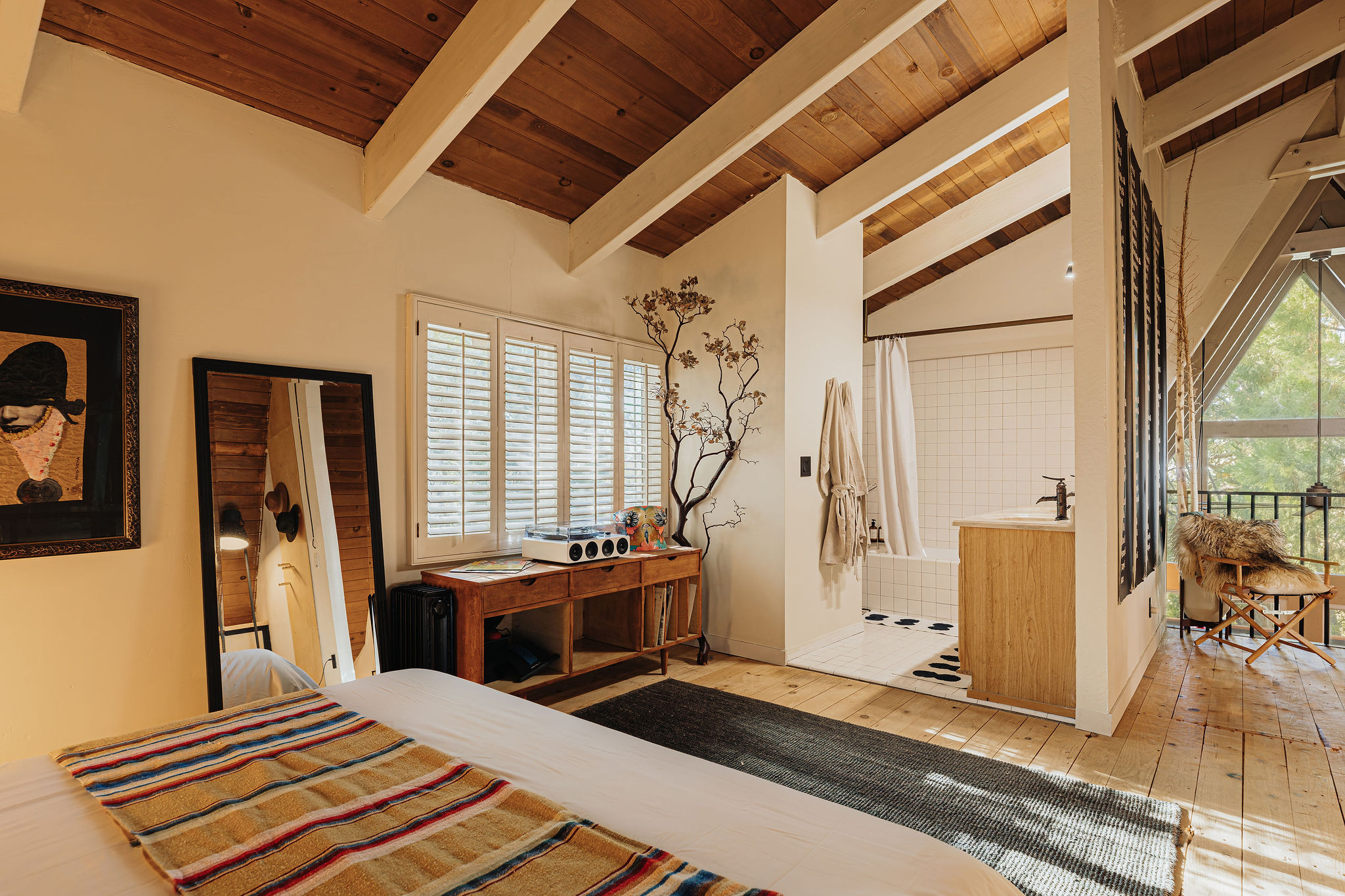 Sunlit bedroom with wood-beam ceilings, ensuite bath, and balcony