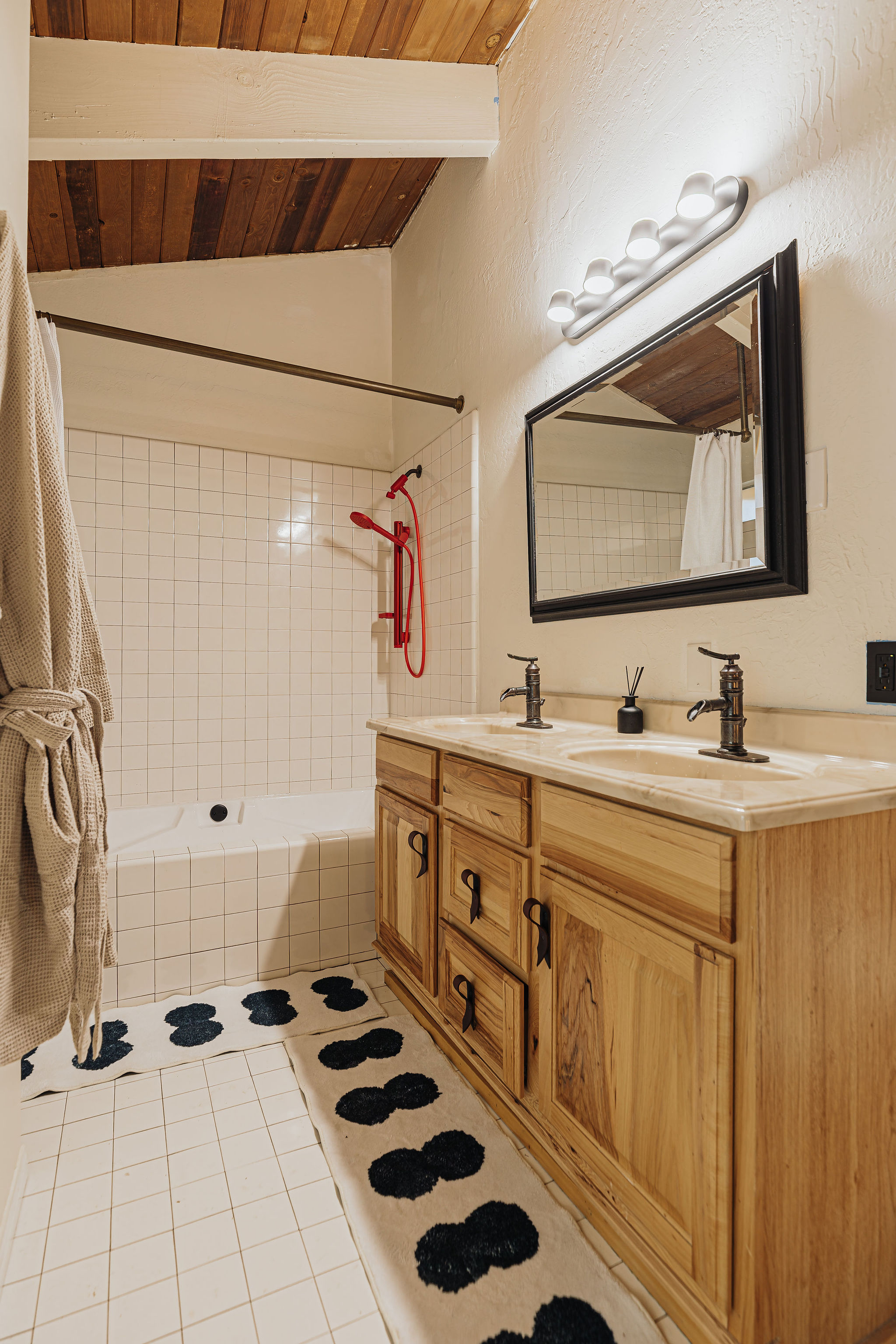 Rustic double-vanity bath with wood ceilings and stylish red shower accents