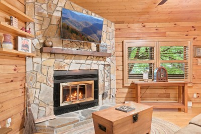 A closer look at the stone hearth: mounted TV above a reclaimed mantel, a tree-framed window across the room, and the WiFi card sitting on the console table next to the vintage radio.