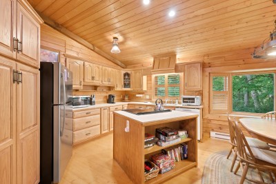 Pine cabinets wrap the kitchen from floor to ceiling, the island doubles as game night headquarters with shelves of board games, and the windows over the sink look straight out into the trees while the round table waits nearby.