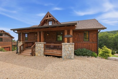 Cedar shake siding and a timber-frame gable set the tone at Peak a View, where stone-clad porch posts frame rocking chairs on the covered entry — first impressions of forested High Country hillsides before you're even through the door.