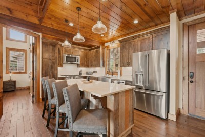 Glass pendants light the reclaimed-wood ceiling over a quartz-topped island with seating for four, while stainless appliances — French-door fridge, gas range, built-in microwave — round out this working mountain kitchen.