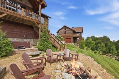 Adirondack chairs circle the stone fire pit just steps from the private hot tub, tucked into Peak a View's sloped mountain lawn with a timber staircase climbing back to the main deck — outdoor evenings built right in.