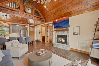 A timber-railed loft overlooks this great room from above, the stone fireplace anchoring a space that opens straight through to the kitchen and front entry.