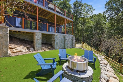 Four Adirondack chairs circle the stone fire pit on the turf lawn, s'mores and stargazing, no matches required.