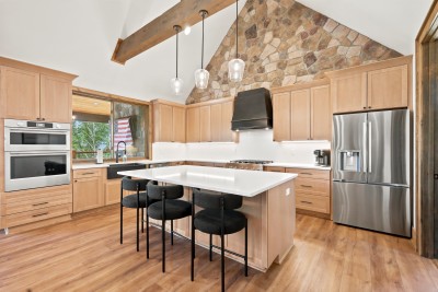 A commercial-style gas range, stone hood surround, and stainless fridge keep this kitchen ready for a real family dinner, with the wet bar just through the doorway.