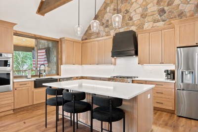 The vaulted, stone-backed kitchen centers on a massive quartz island with seating for six, gas range, double ovens, and a farmhouse sink make it as functional as it is beautiful.