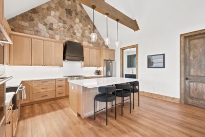 Stone walls, a black range hood, and a six-seat quartz island make this vaulted kitchen the heart of the home.