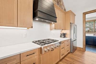 Kitchen counter with a stainless gas cooktop, black shiplap range hood, marble-look backsplash, coffee maker, stainless refrigerator, and a doorway to a navy-cabinet wet bar.