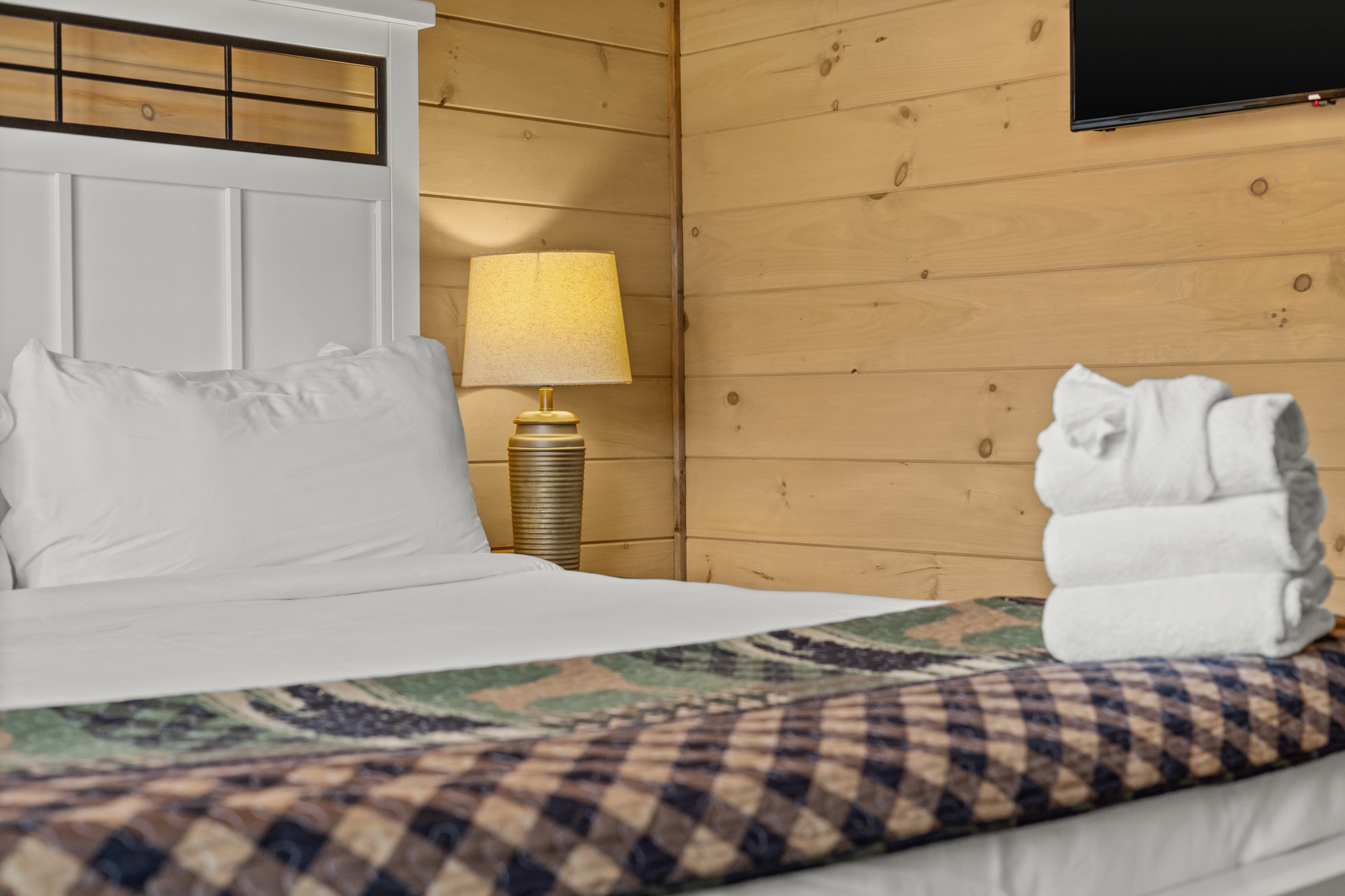 Cozy wood-paneled bedroom with plush linens, warm lighting, and TV