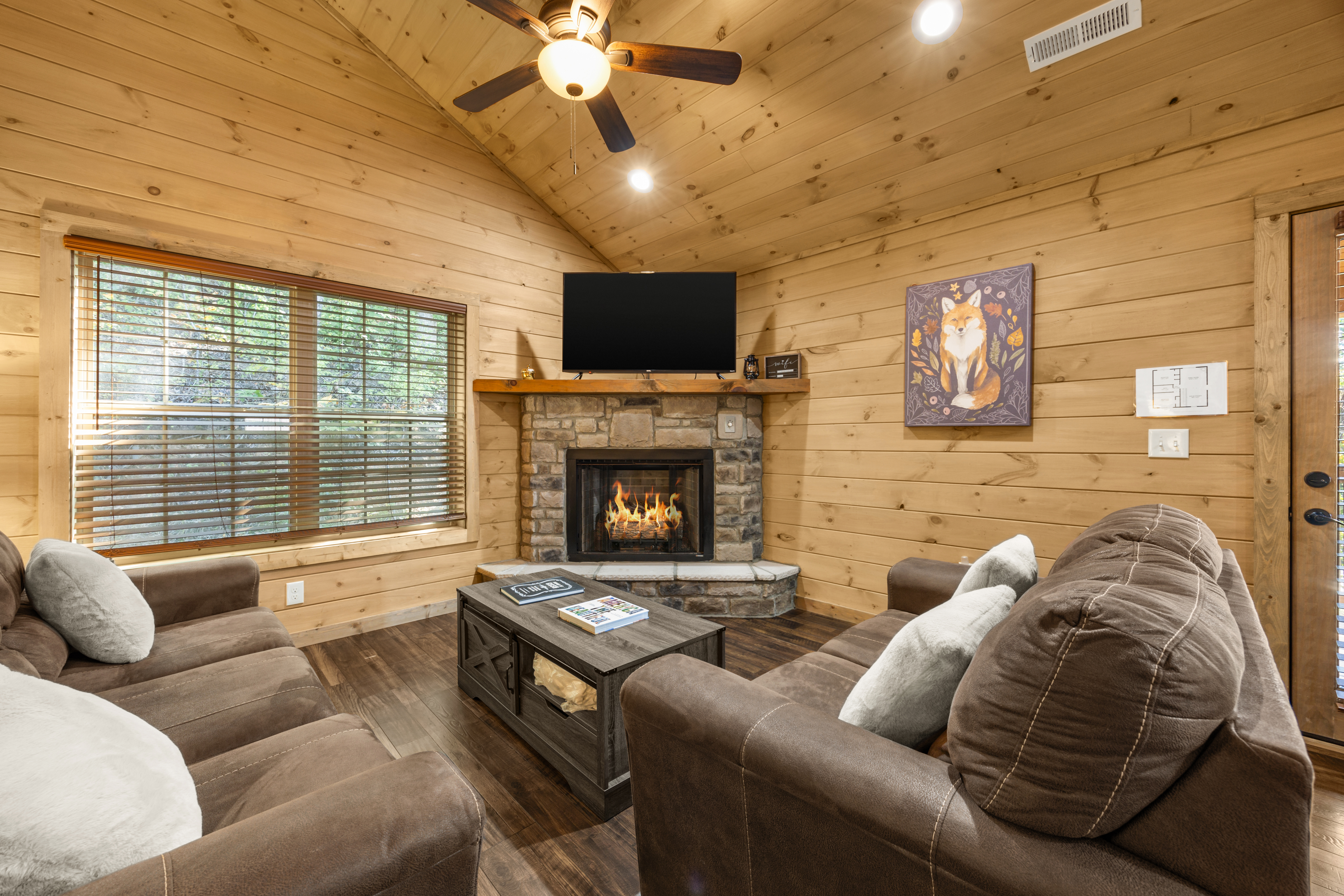 Cozy cabin living room with stone fireplace, TV, and vaulted wood ceilings