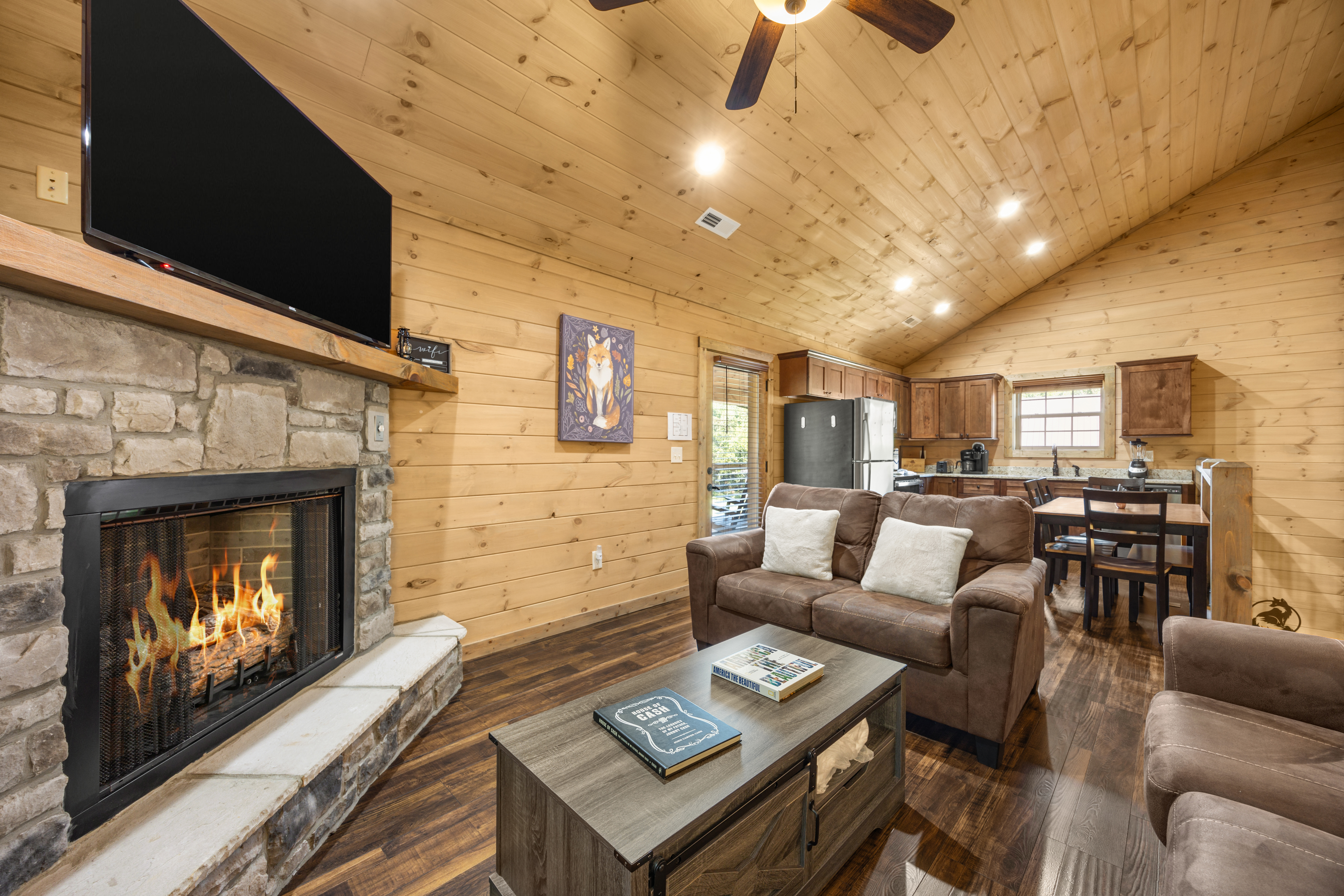Cozy cabin great room with stone fireplace, TV, and open kitchen