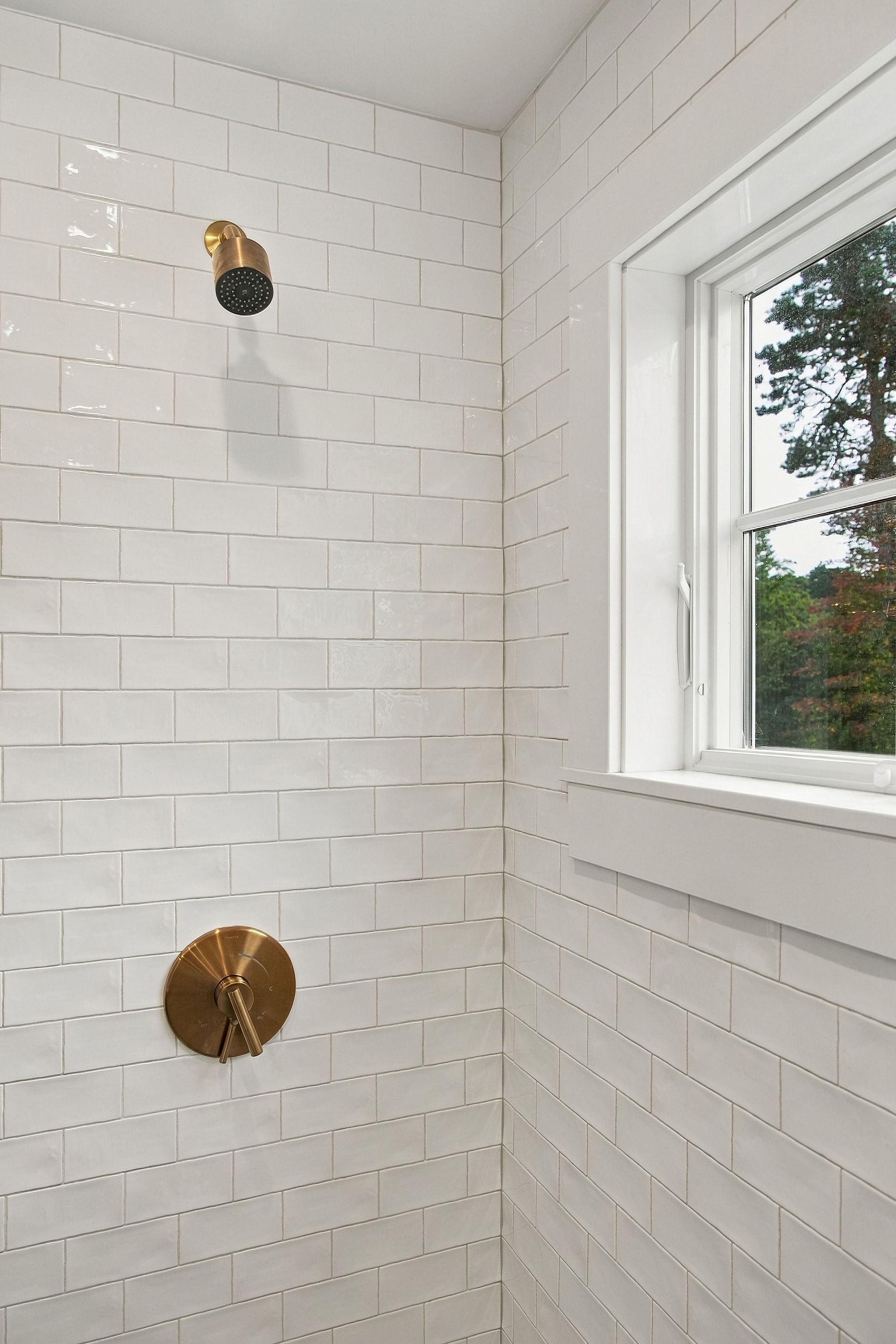Bright tiled shower with brass fixtures and a sunlit window view
