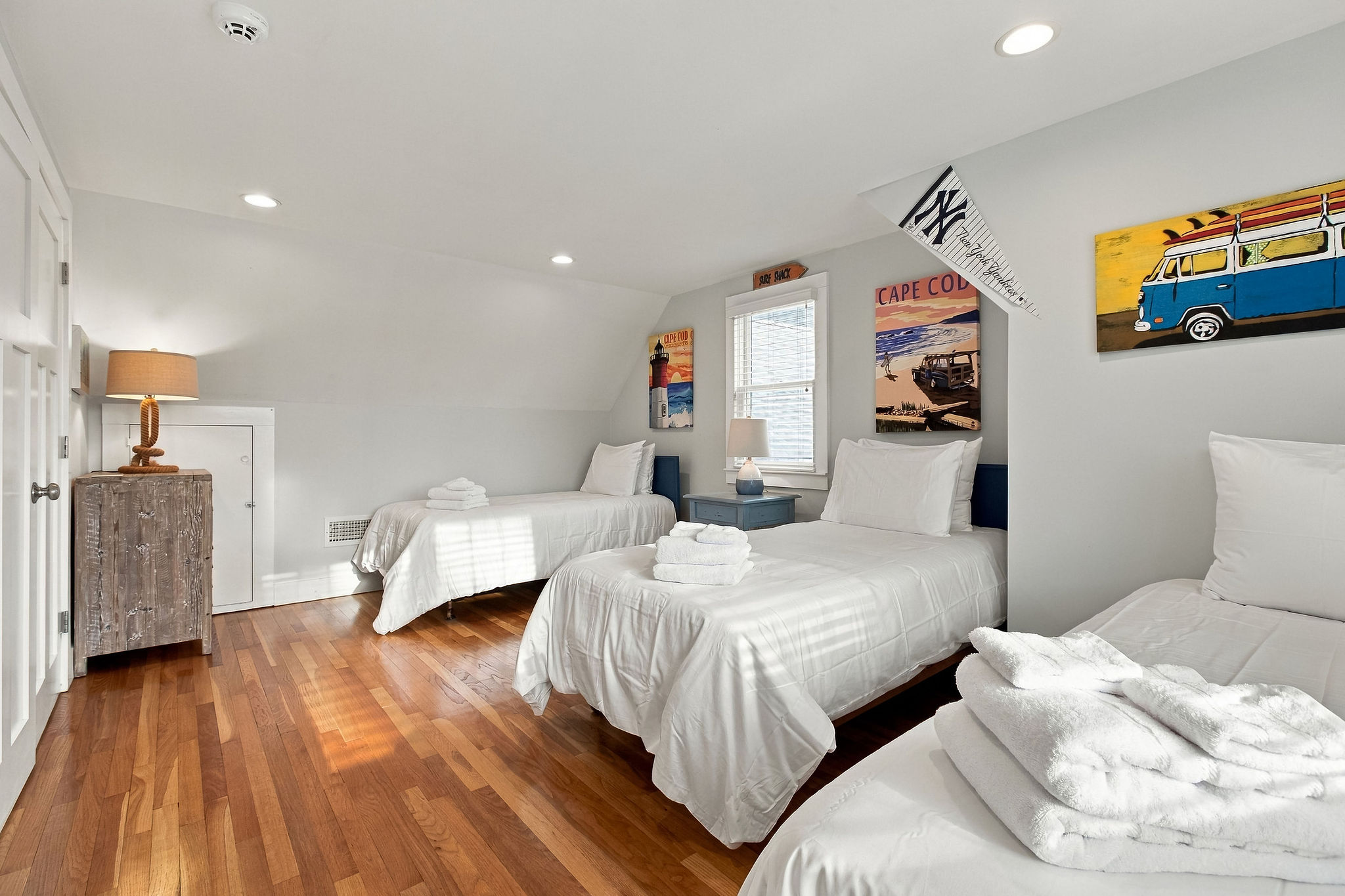 Bright coastal bunk room with 3 twin beds and sunny hardwood floors