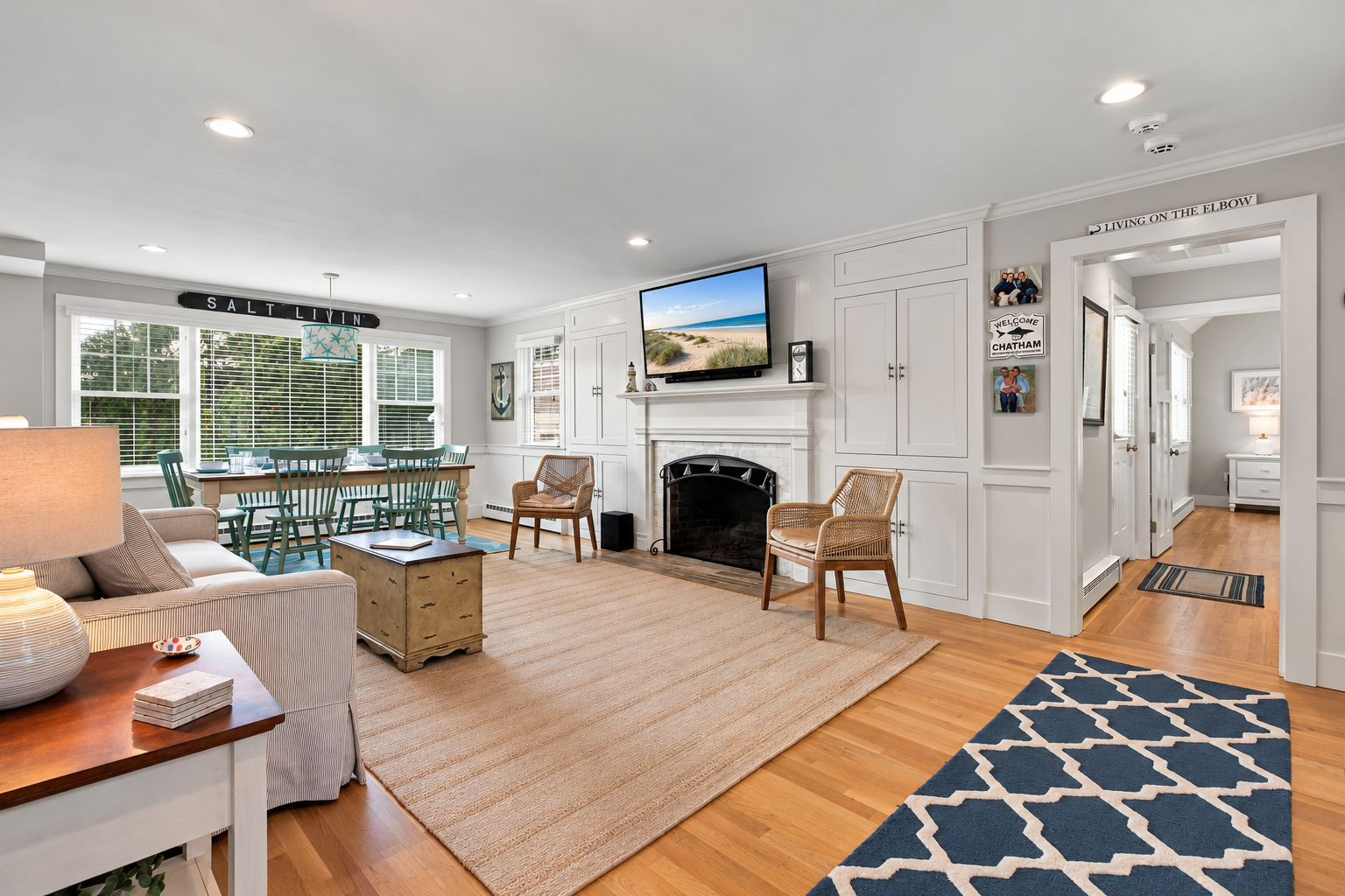 Bright coastal living room with fireplace, TV, and sunny dining area