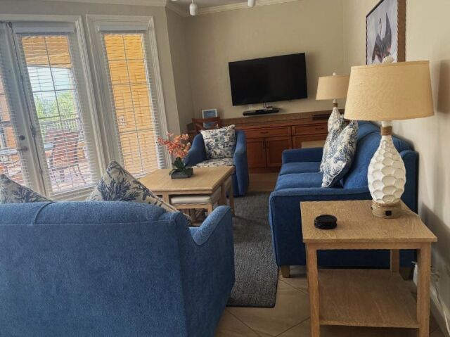 Bright coastal-style lounge with plush seating, large TV, and patio access