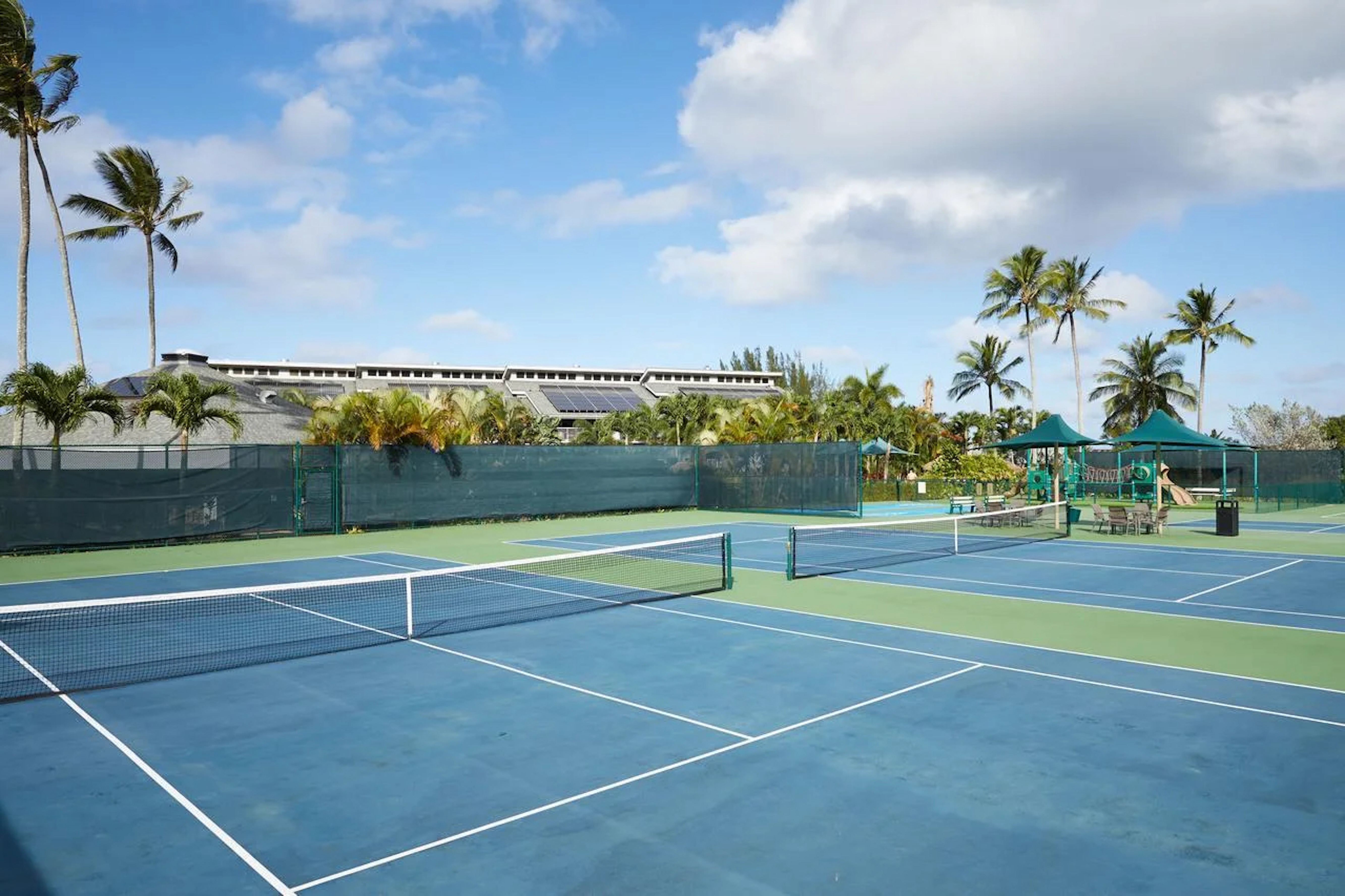 Resort-style tennis courts with palm views and shaded seating