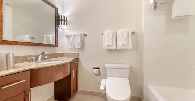 Bright bathroom with granite vanity, tub-shower combo, and fresh towels