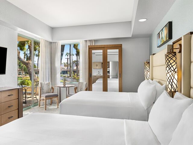 Bright double-queen room with patio access, resort views, and cozy seating