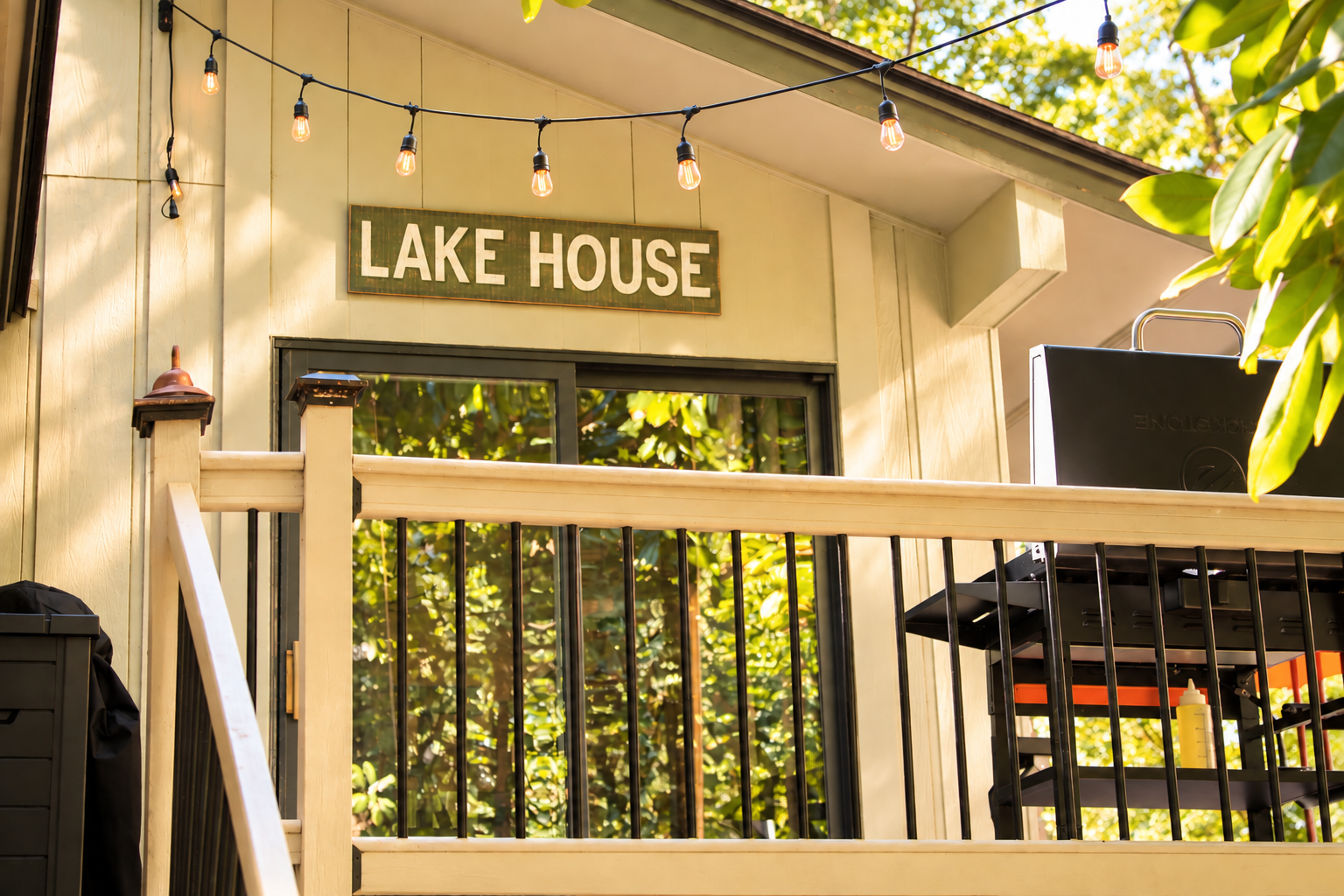 Cozy lake house deck with string lights, grill, and wooded views