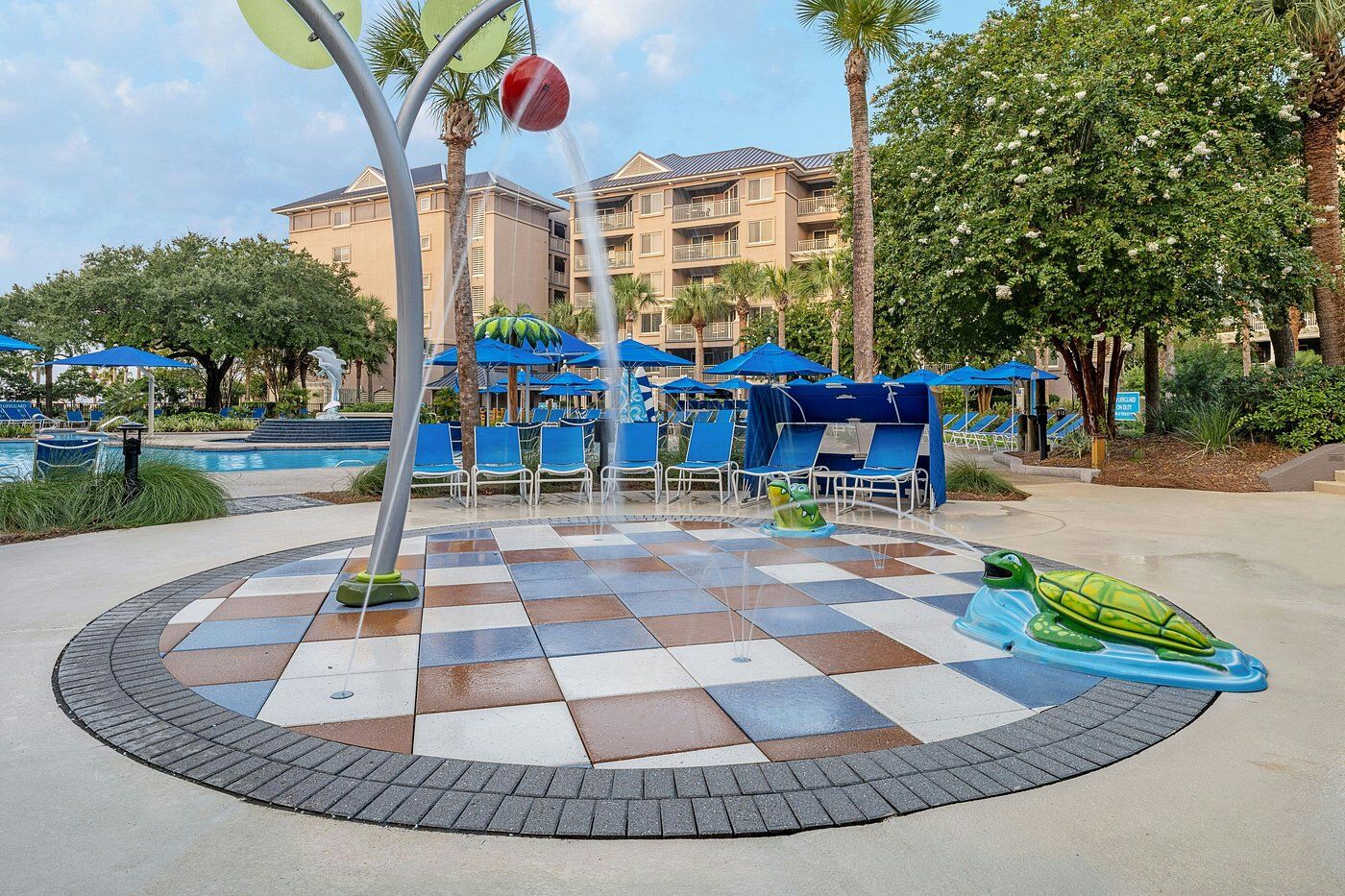 Resort-style pool deck with family splash pad, palms, and shaded loungers
