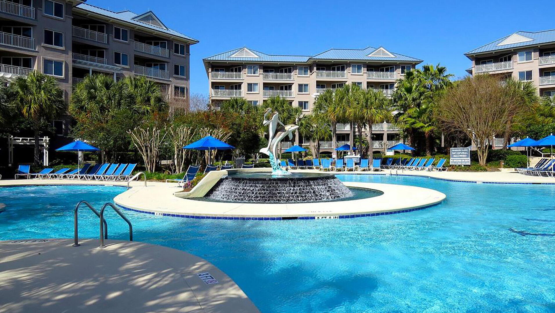 Resort-style pool with fountain, loungers, and sunny tropical vibes