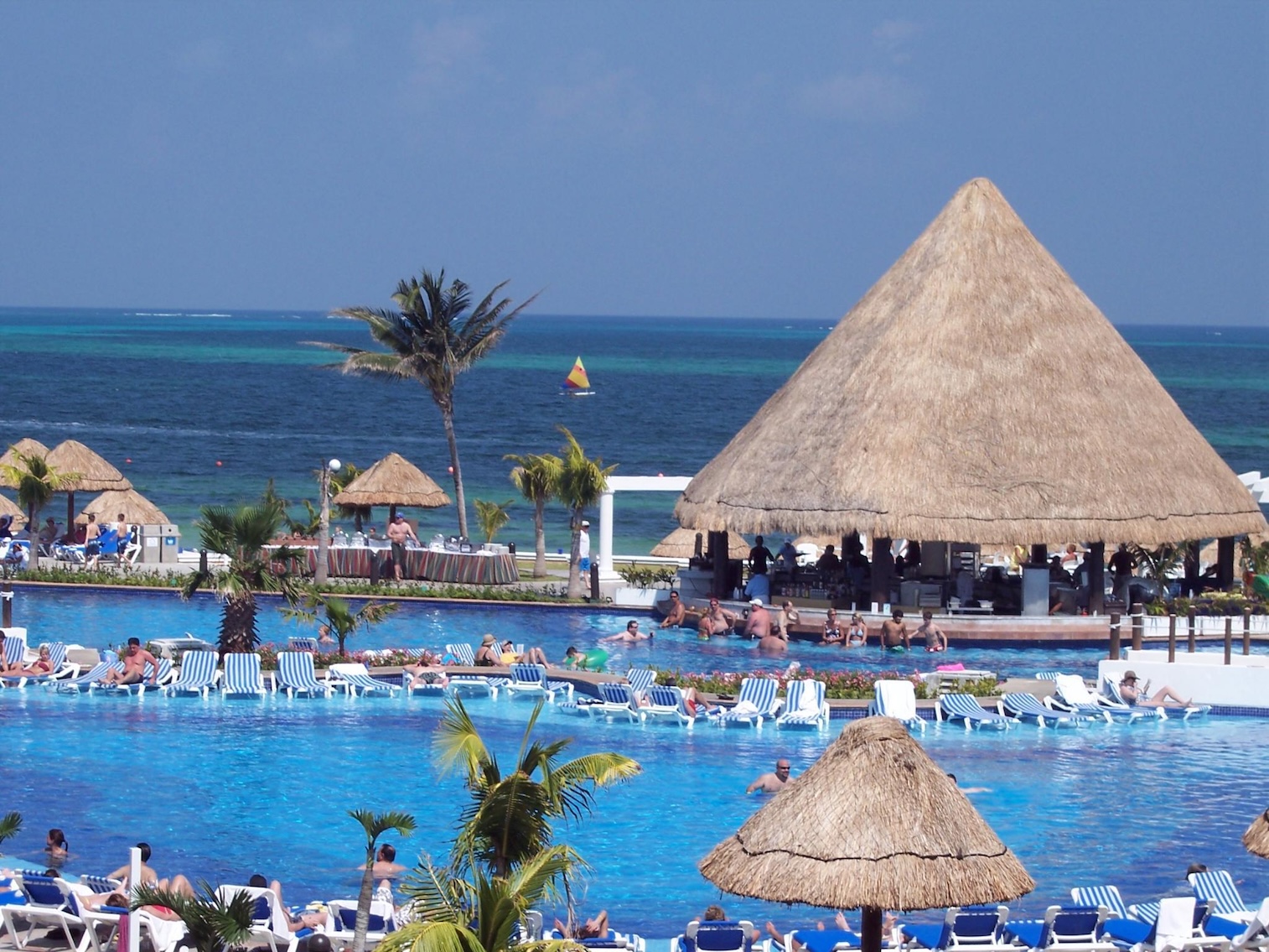Oceanfront resort pool with tropical palapa bar and ample lounge seating